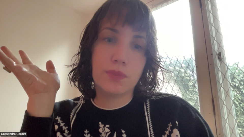 Cassie on a Zoom call, hand raised mid-gesture, looking incredulous